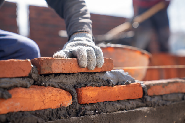 bricklayer-industrial-worker-installing-brick-masonry-with-trowel-putty-knife-construction-site_33835-1135