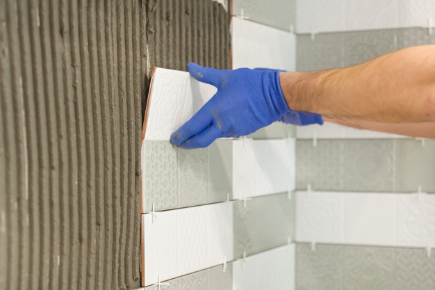 closeup-tiler-hand-laying-ceramic-tile-wall-kitchen_116407-1666